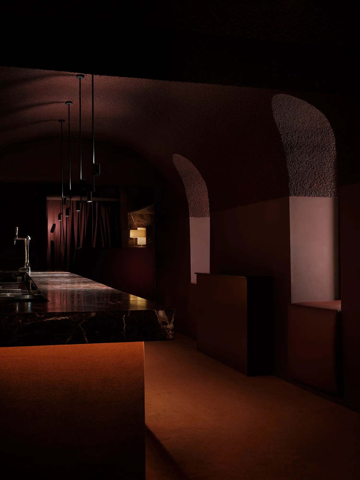 Dark modern bar with a marble counter, brown color scheme, and dim lighting