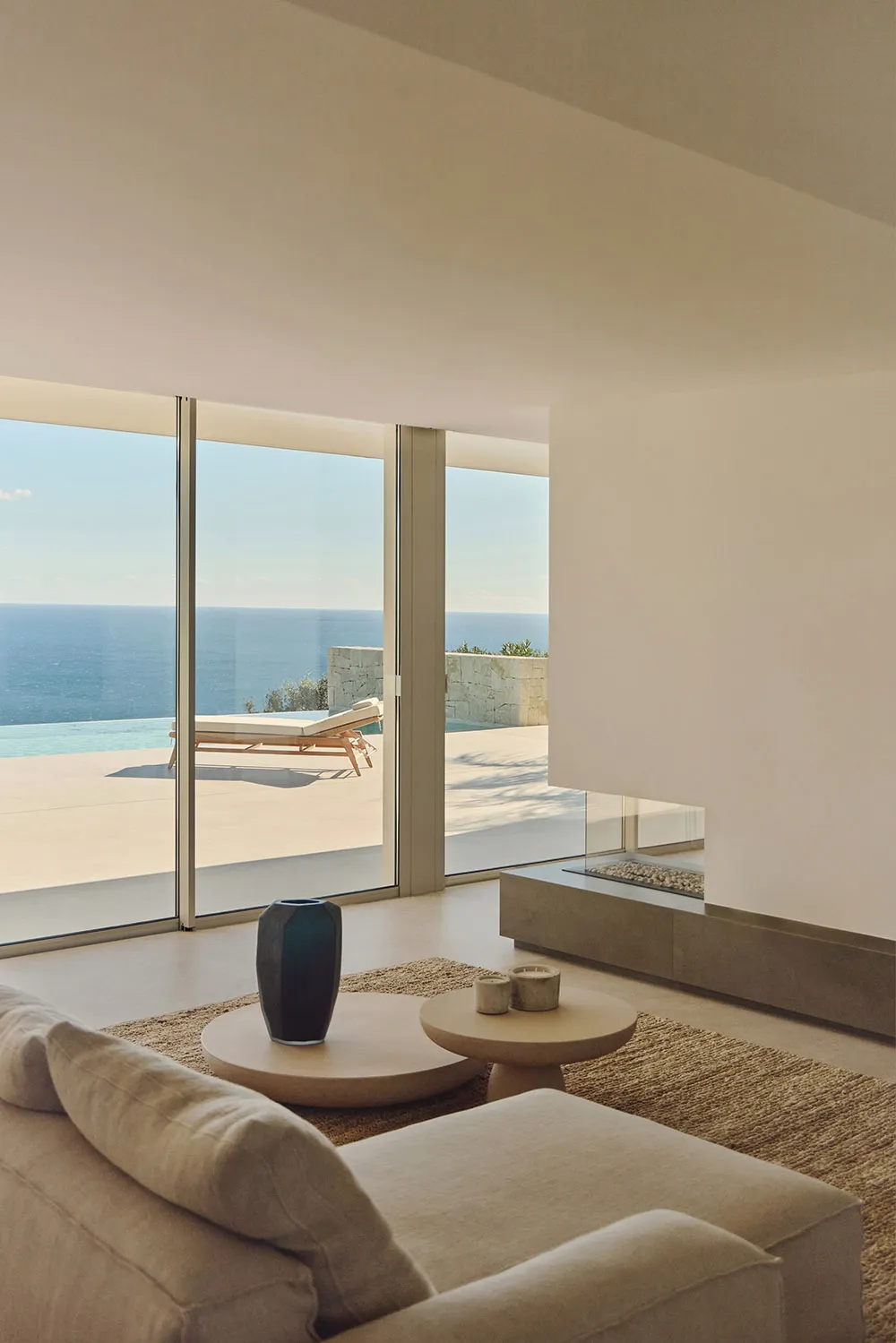 Coastal living room with a couch, chair, dining table, and fireplace, filled with natural light from a large window overlooking the ocean