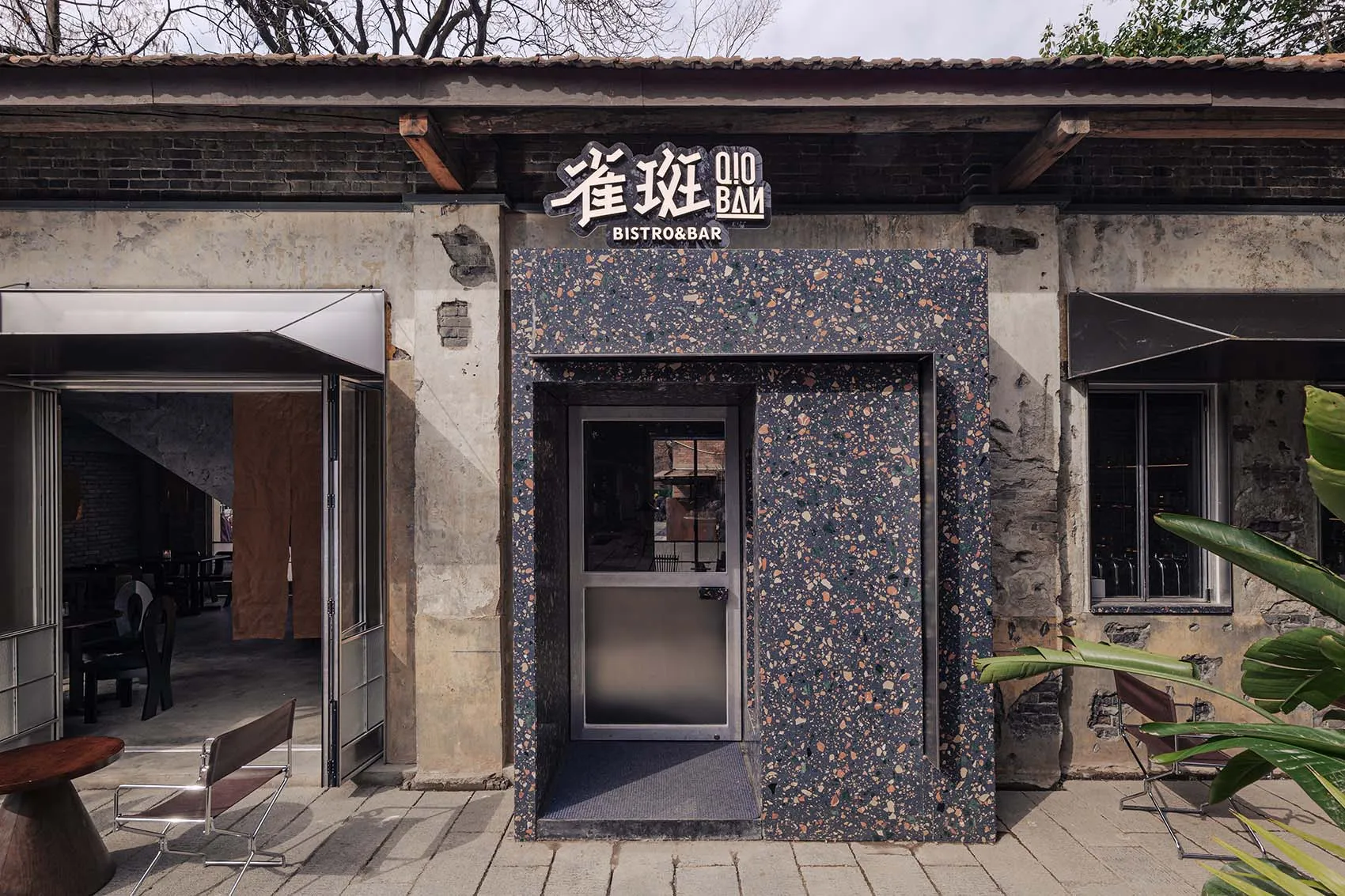 Outdoor restaurant with a stone exterior, a stone wall, and a stone door, set in a natural environment with earthy tones and natural lighting