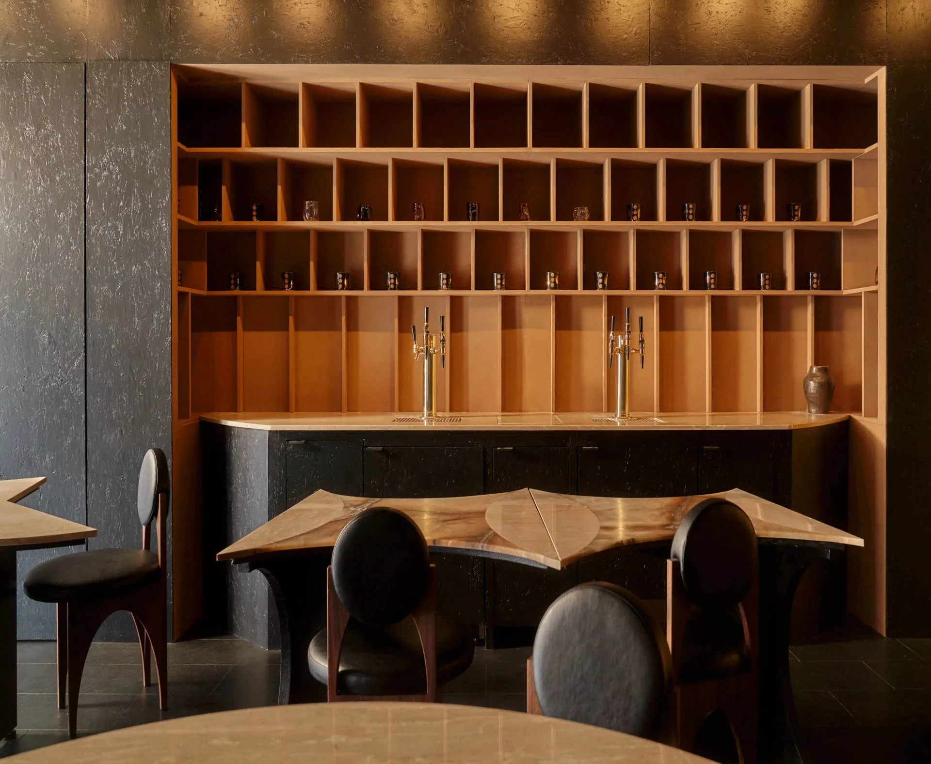 A bar area with a wooden counter, multiple chairs, and a dining table, featuring a well-equipped bar with bottles and wine glasses, creating an inviting and comfortable atmosphere