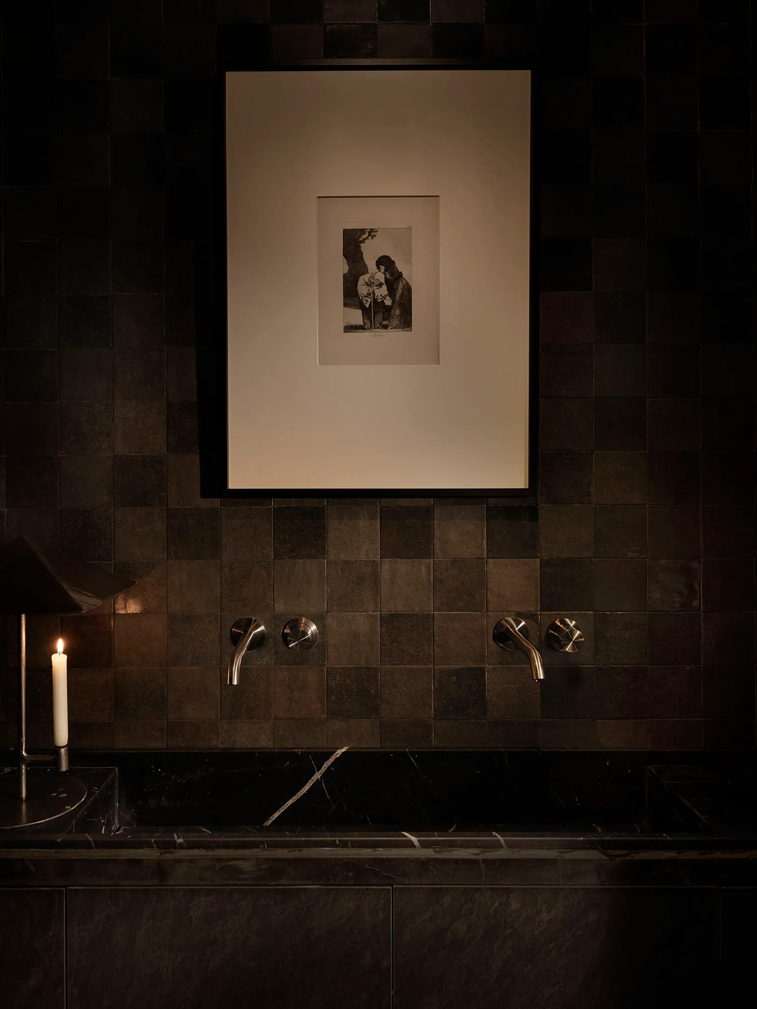 A vintage bathroom with a black and white marble bathtub and tile floor, featuring a sink and a picture above the tub, in a dimly lit space