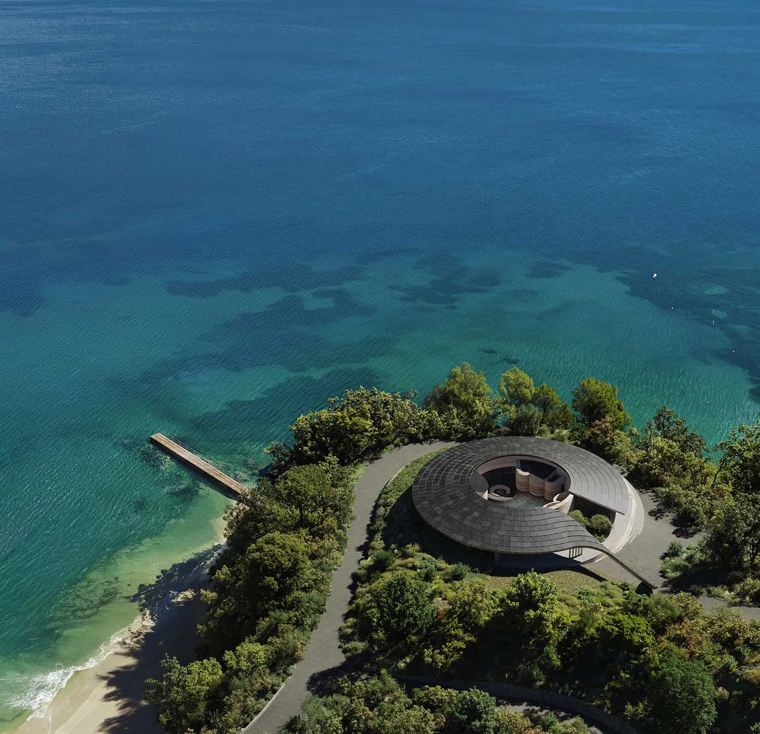 A modern house on a hillside overlooking water, surrounded by trees, with a circular structure and natural light from windows