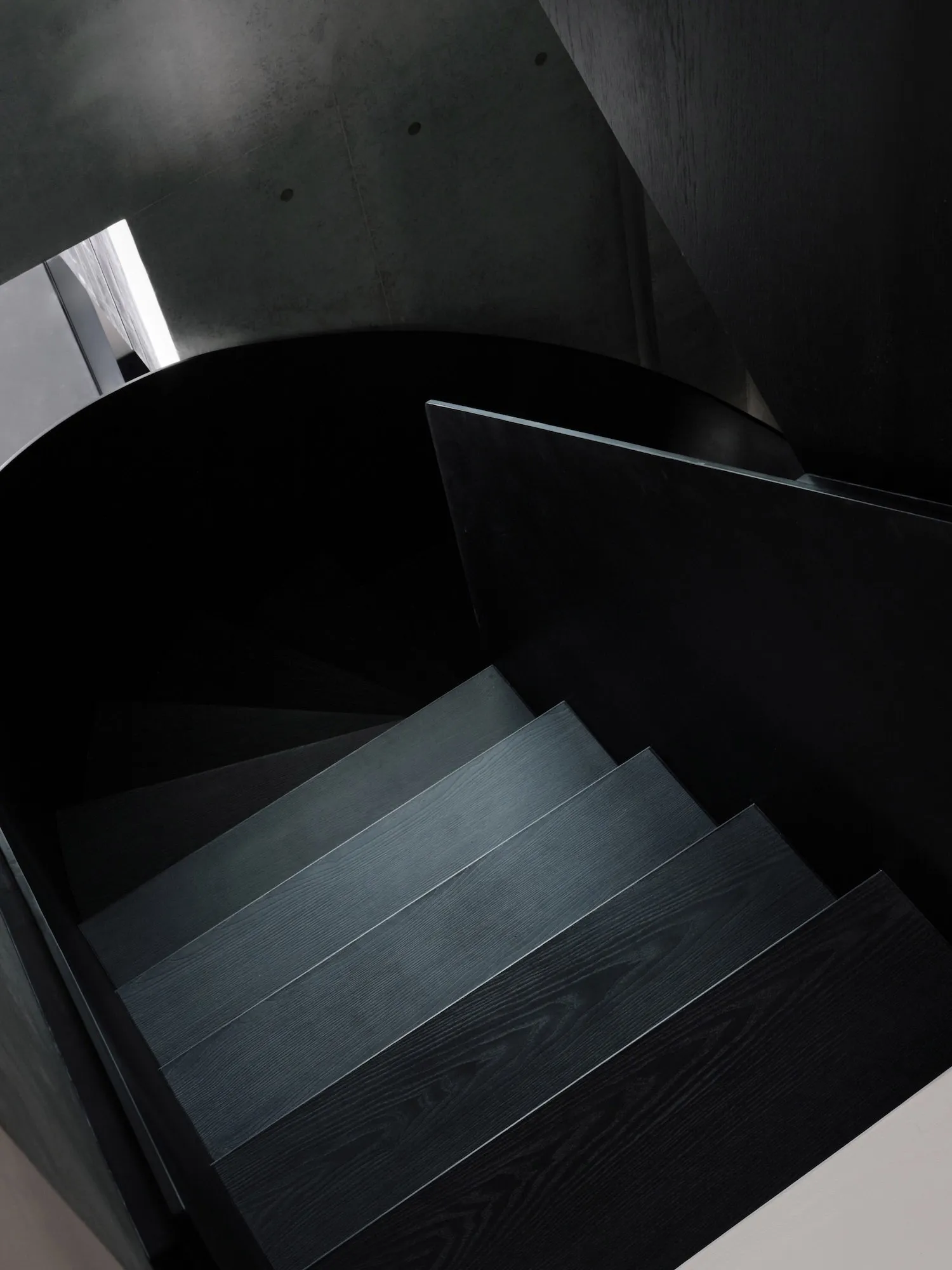 A black and white photograph of a wooden staircase with a metal railing in a dark room, the staircase is the main focus