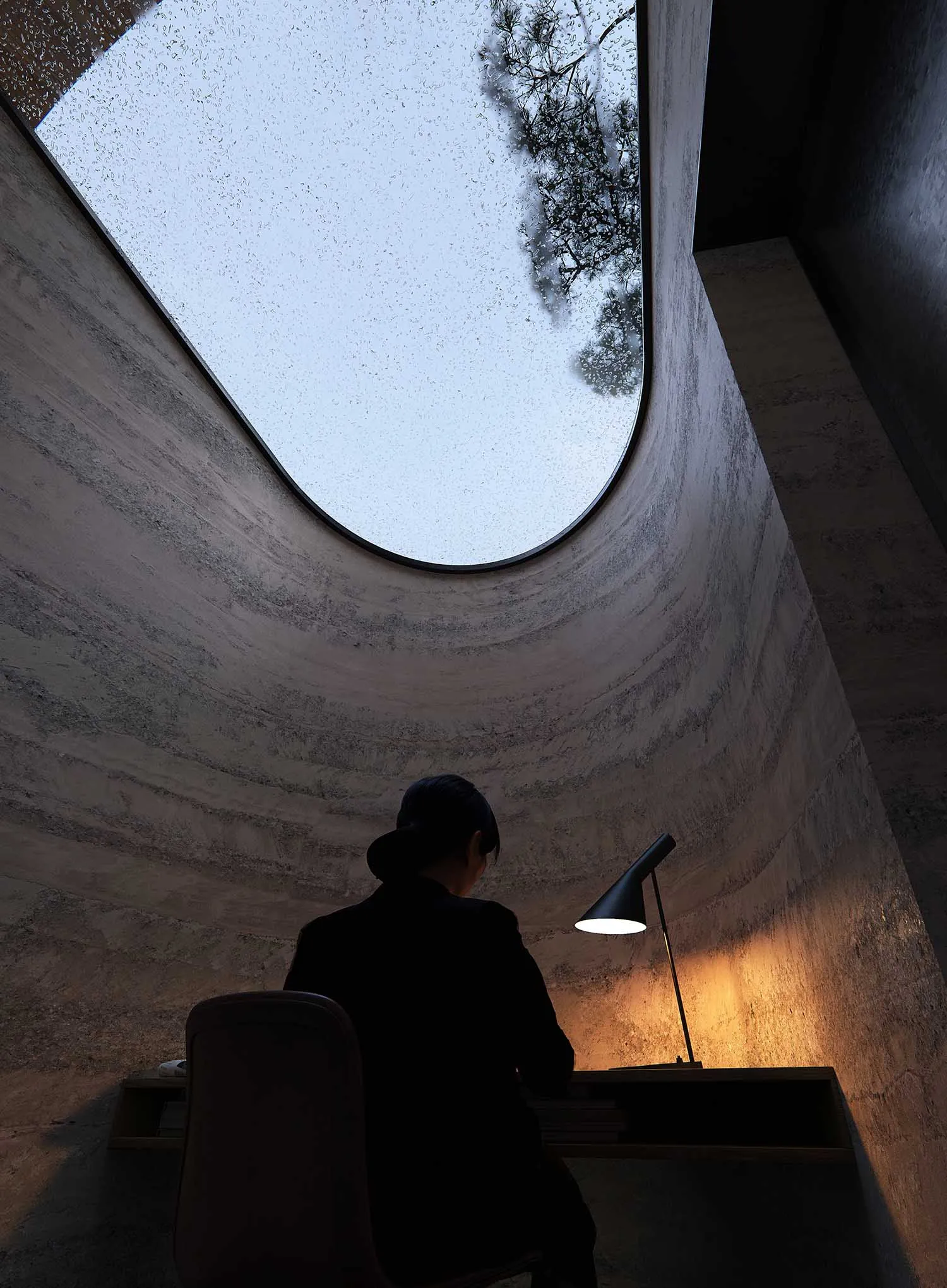一個人坐在木桌前的一個學習環境中，透過窗戶進入自然光線，周圍是 drywall 和中性色彩