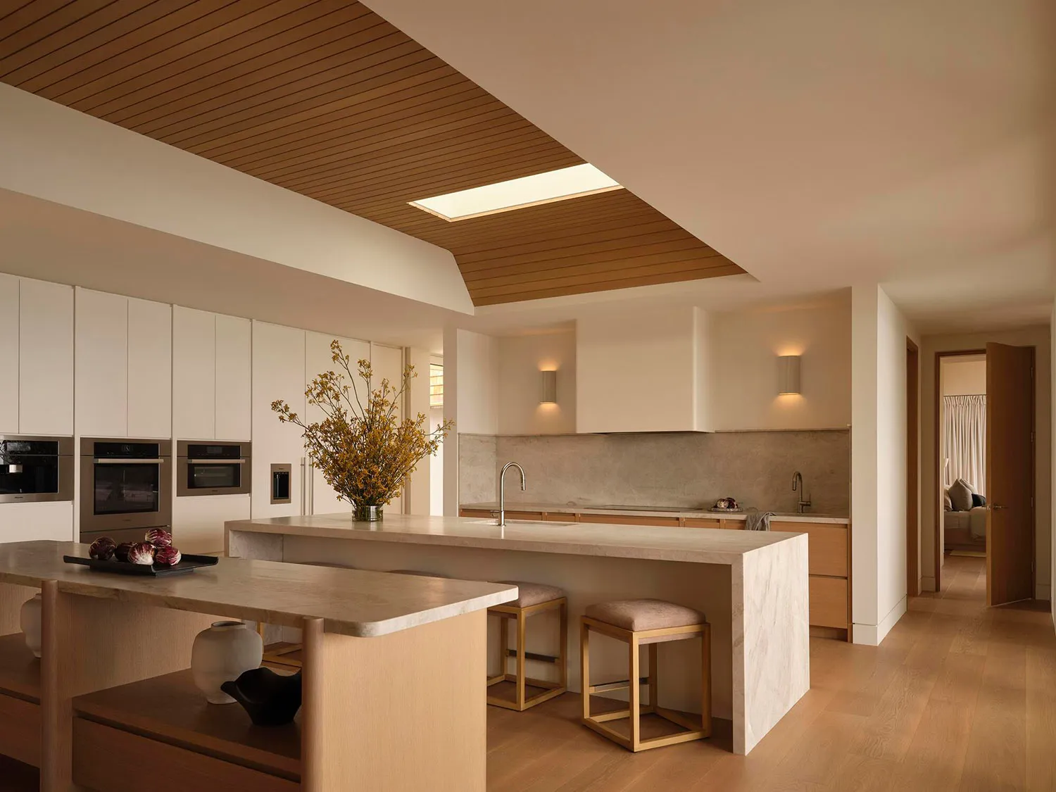 A modern kitchen with a wooden floor and white cabinets, featuring a sink, refrigerator, and microwave, with dim lighting creating a cozy atmosphere