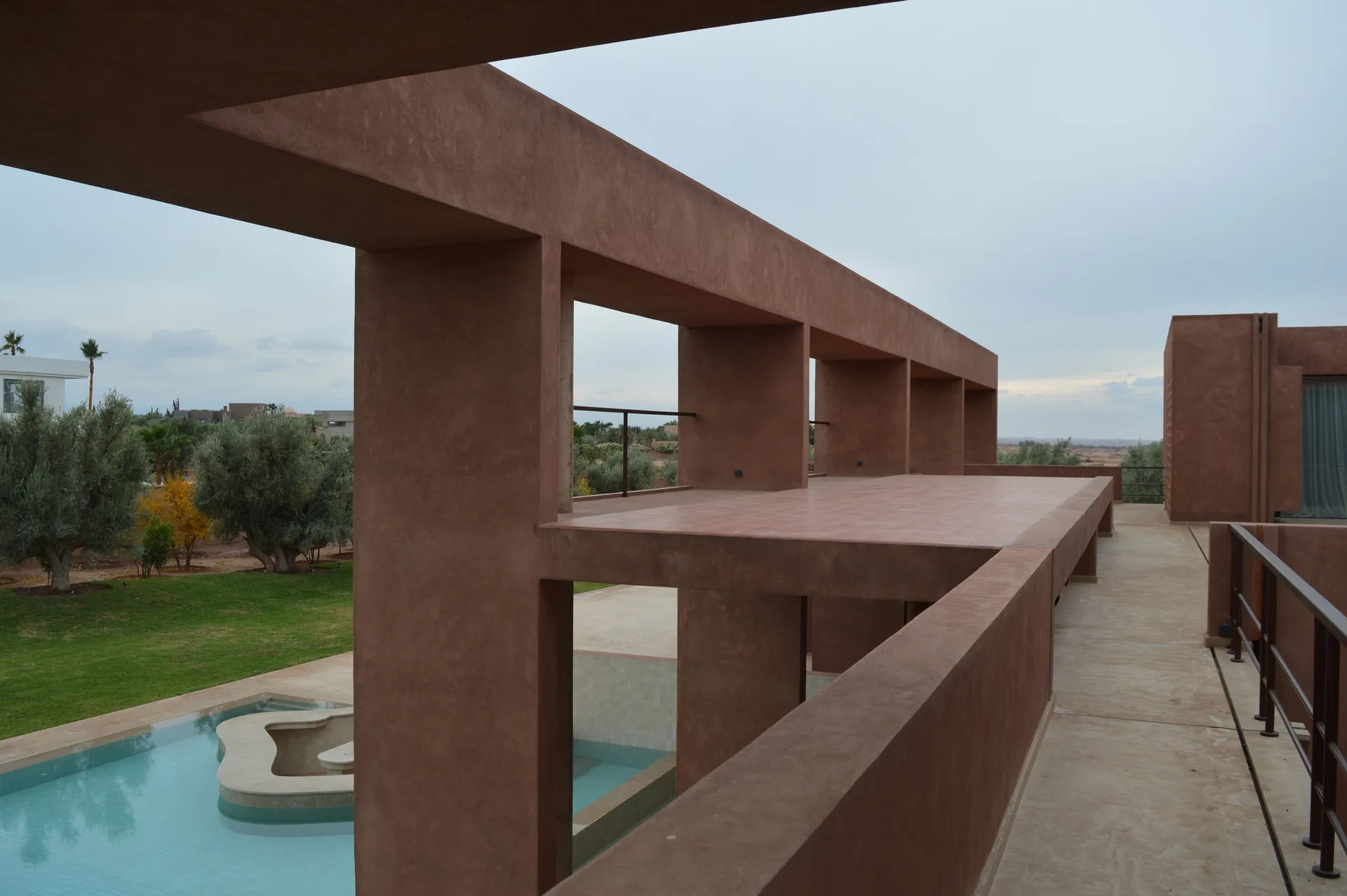 A serene desert villa with a red brick building, a pool surrounded by a concrete structure, and a bench nearby