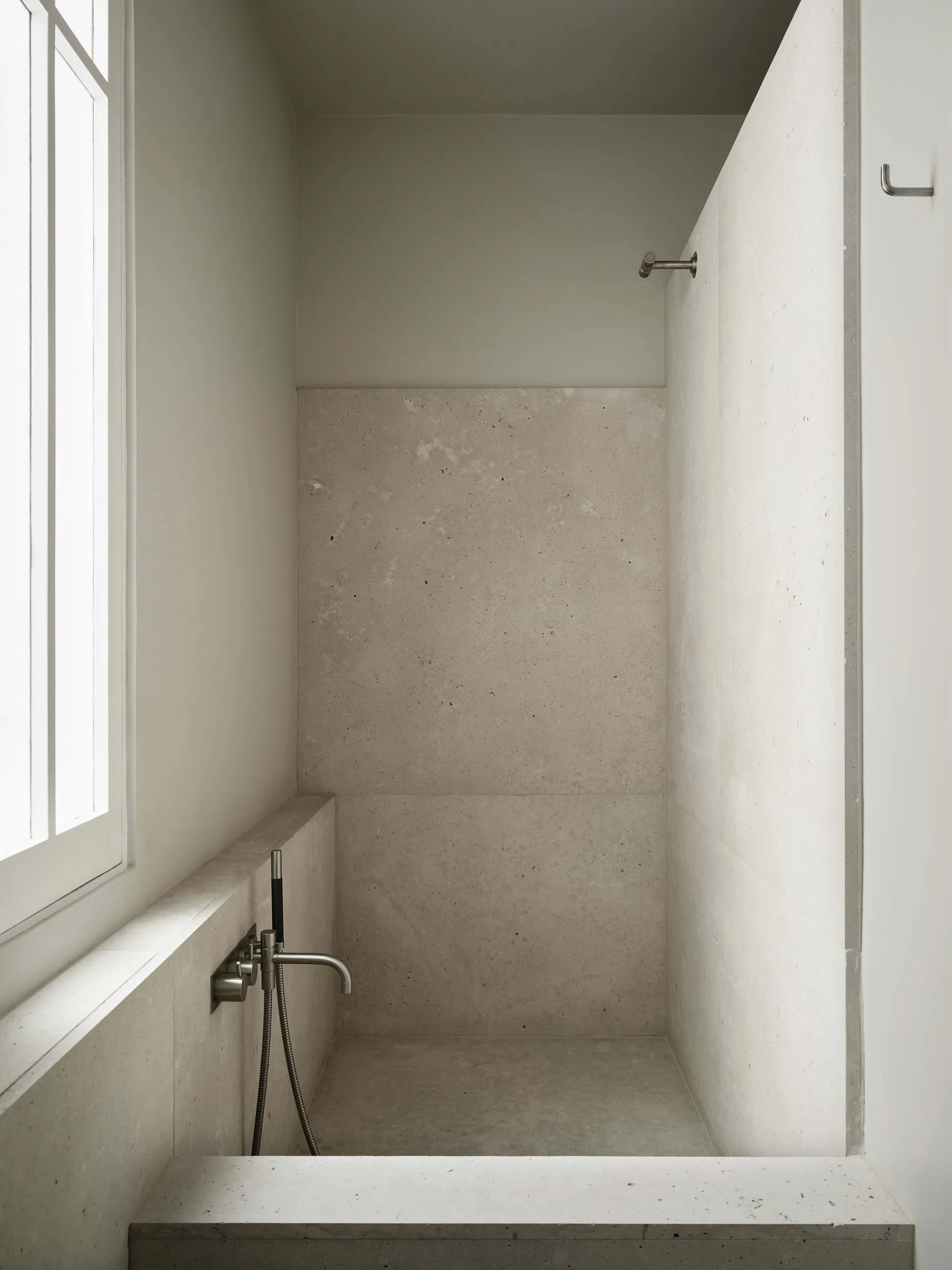 A clean bathroom with a white concrete shower stall and a window, well-maintained and minimalist