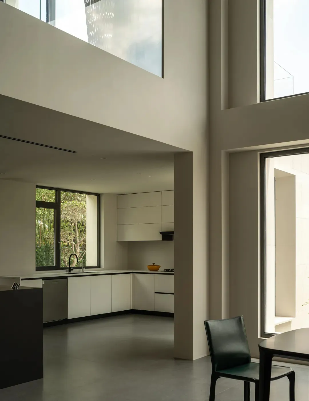 A modern kitchen and dining area with white walls, a dining table, chairs, a couch, and a chair, well-lit by natural light through windows