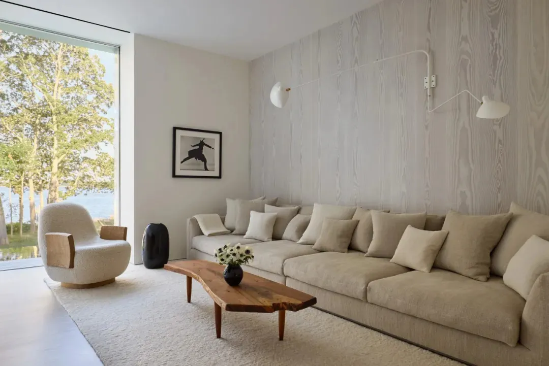 Cozy modern living space with a large couch, coffee table, and potted plants, featuring wood and fabric materials and natural light from a window