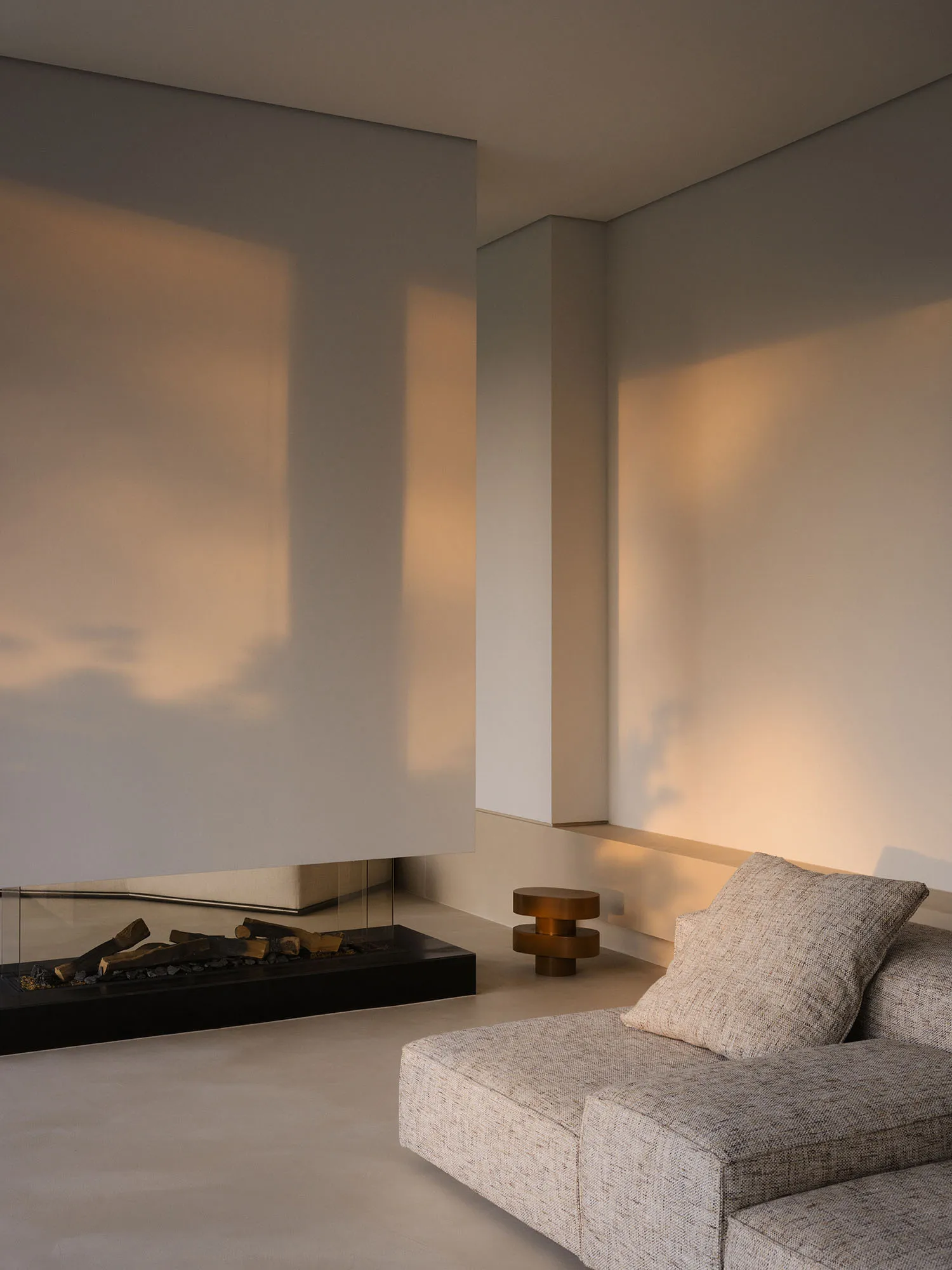 A modern living room with a couch in front of a fireplace, a glass door, and a white wall, lit by natural sunlight