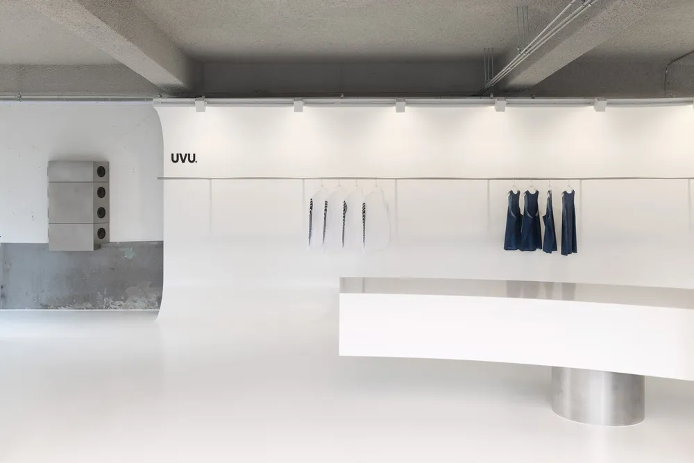 White floor plan of a minimalist retail space with a central counter and surrounding shelves, displaying multiple shirts