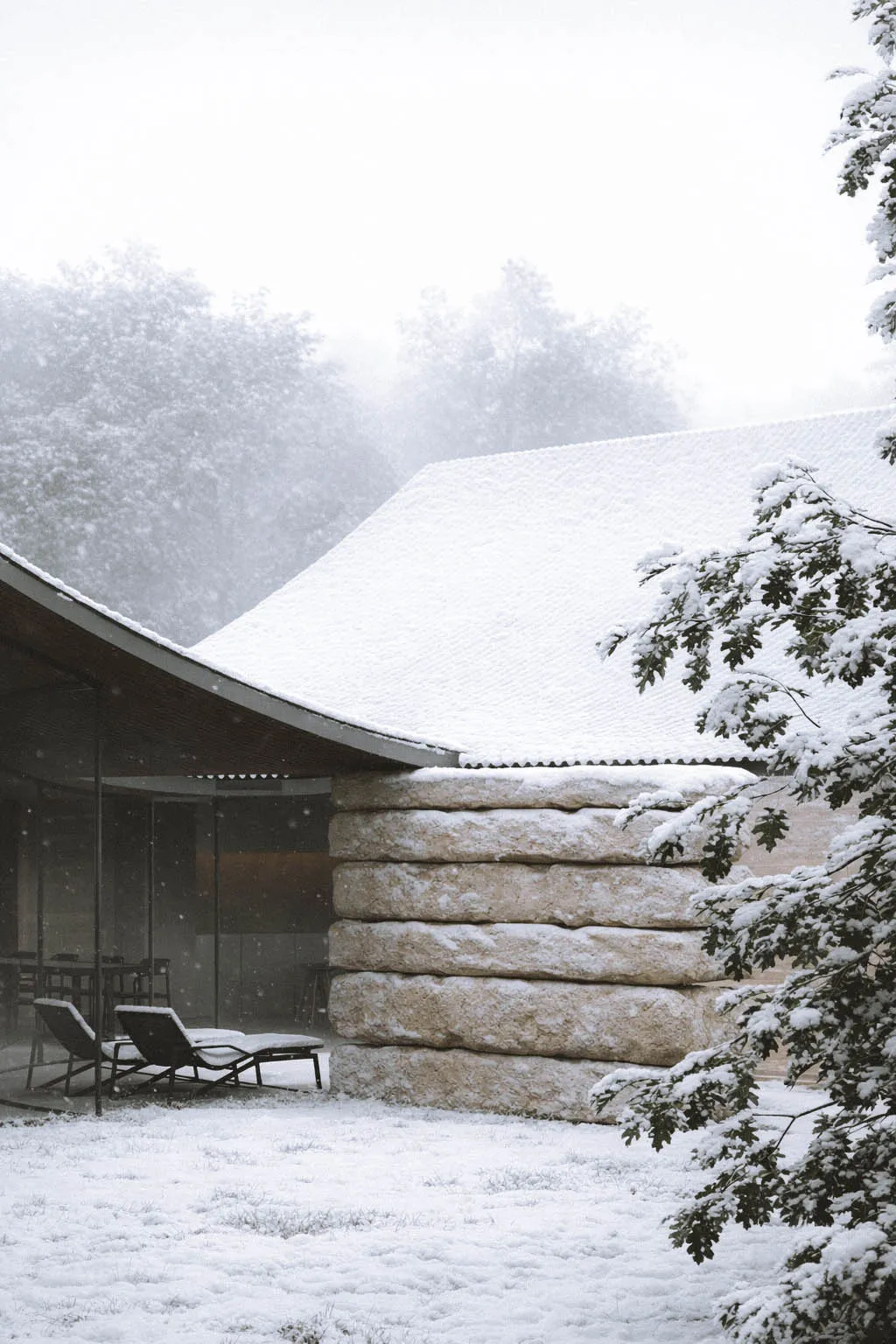 A serene snow-covered house with a curved roof and stone wall, blending modern and traditional architectural styles