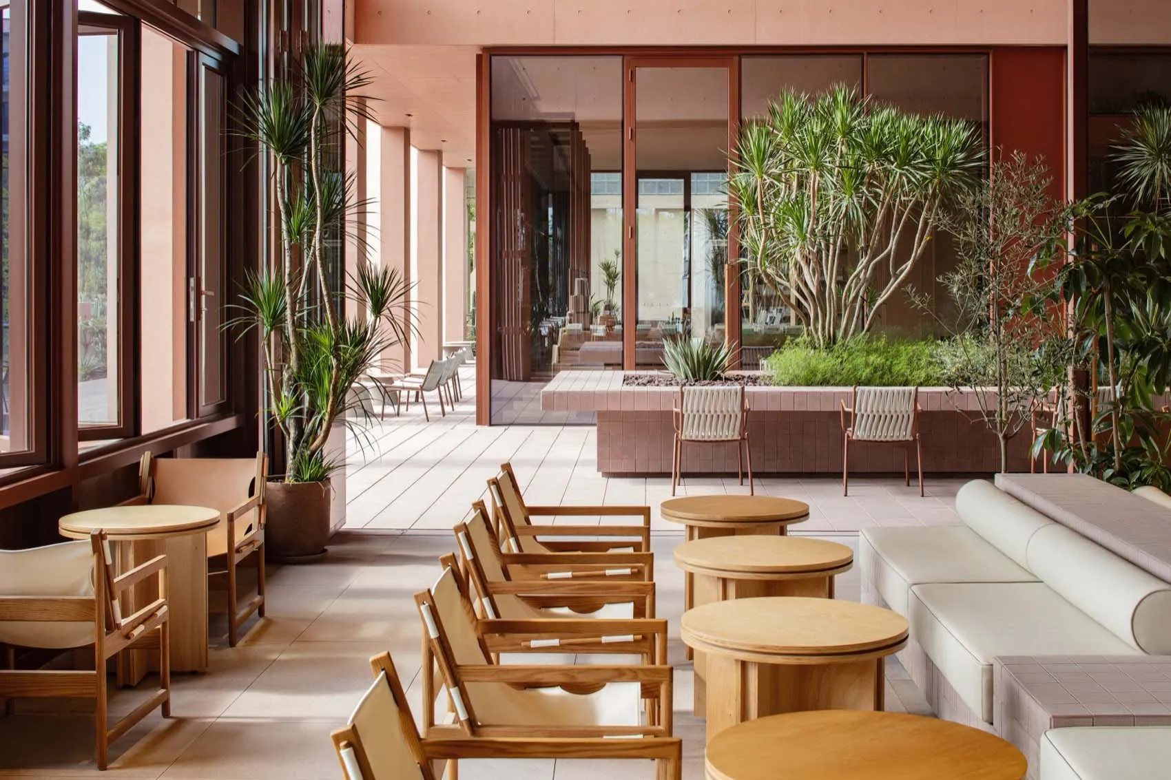 A modern restaurant space with comfortable seating, various chairs, and dining tables, decorated with potted plants and natural light