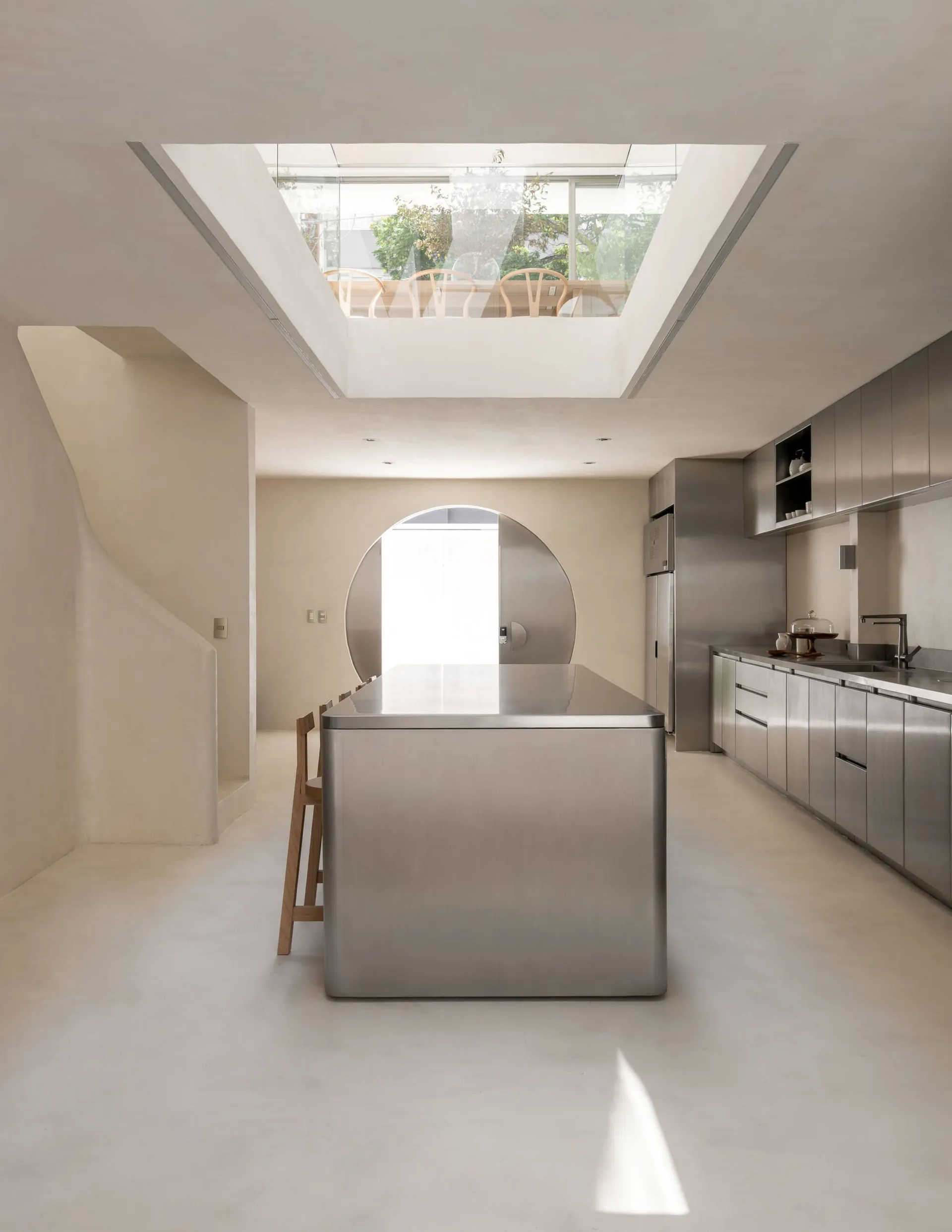 A modern kitchen with a large island, stainless steel countertops, a dining table, and natural light from a window