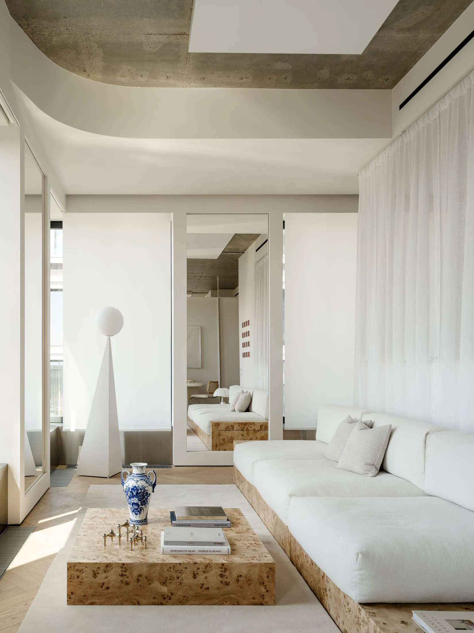 Modern living space with a white color scheme, featuring a couch, chair, dining table, and natural light from windows