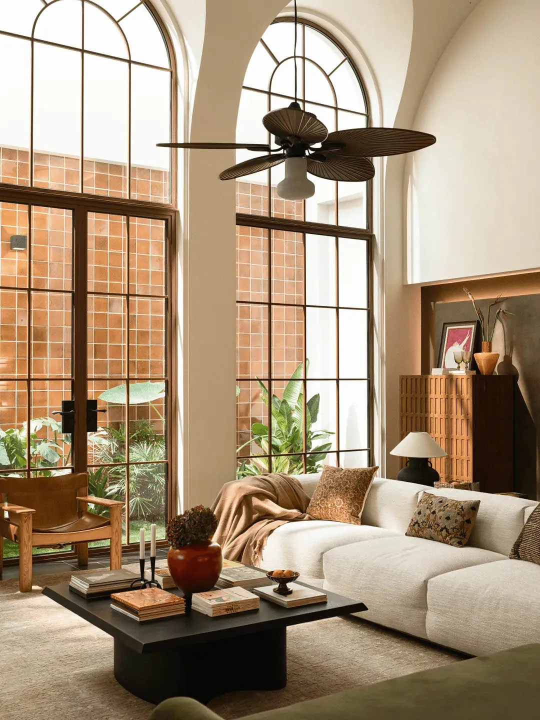 A well-lit living room with a white couch, chair, and dining table, surrounded by furniture and a large fan, creating a comfortable and inviting atmosphere