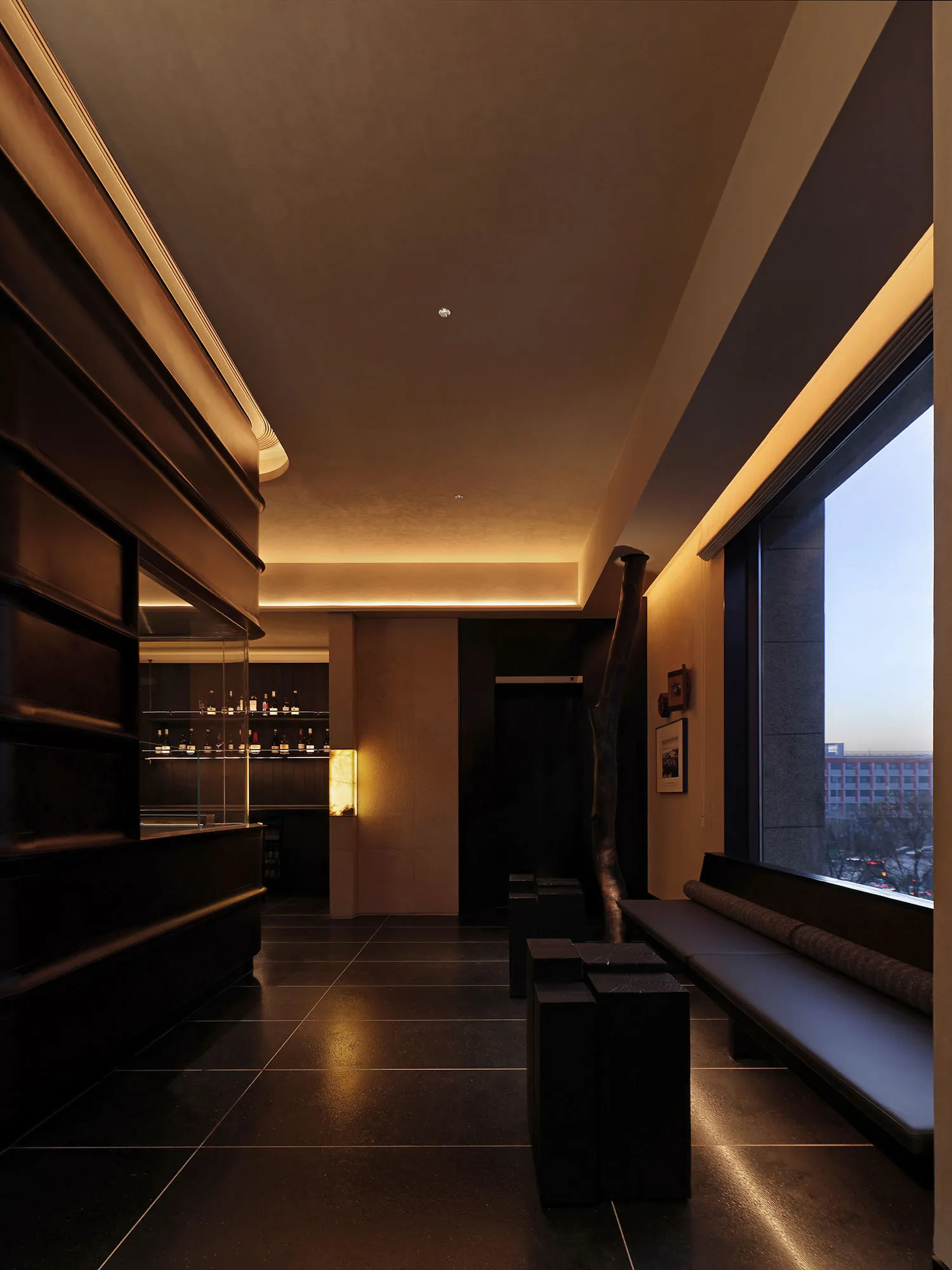 A dimly lit room with a black bench near a window and a bar in the center, featuring a black and white color scheme and sleek, contemporary design