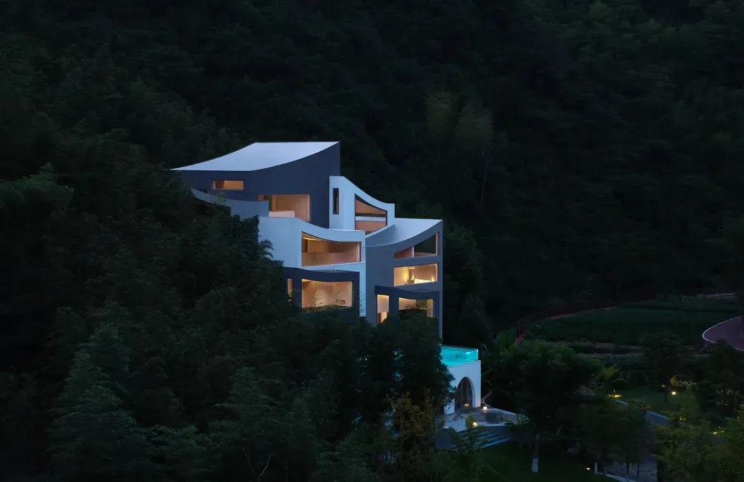 A serene and picturesque modern house with a swimming pool, surrounded by trees and mountains, featuring a mix of white and gray elements