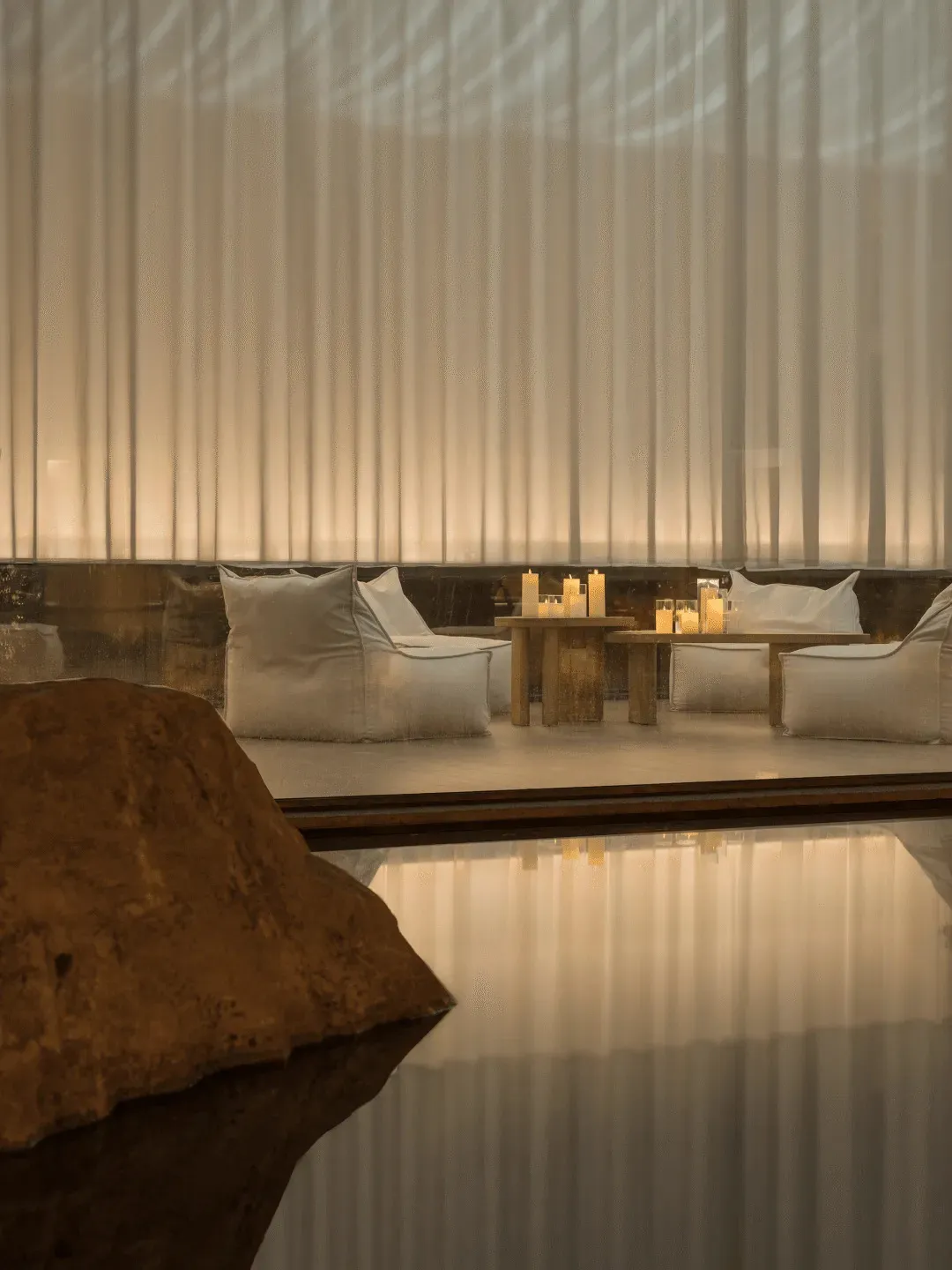 A modern dining space with a wooden table and chairs, surrounded by candles and natural light from a nearby window