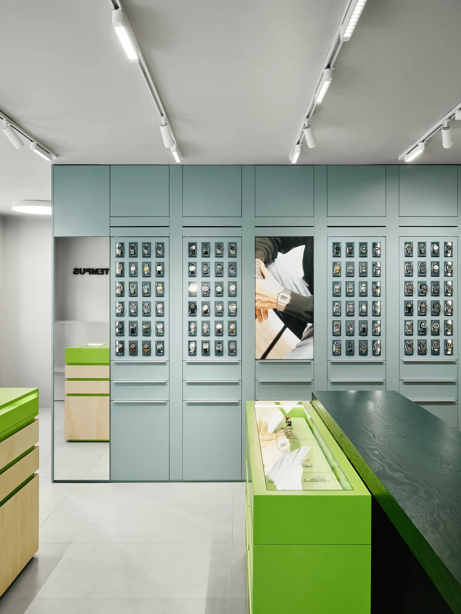 A modern store display showcasing watches and other items with a green color scheme and well-executed lighting