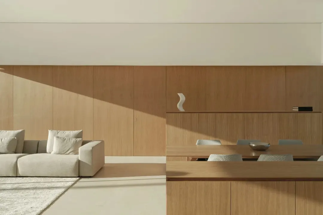 A modern living and dining area with a wooden floor, white walls, and natural light, featuring a couch, chair, dining table, and chairs with a bowl on the table
