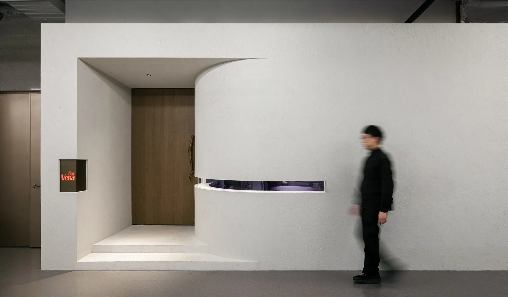 A small, modern room with a white door and wall, open to a bright and clean hallway