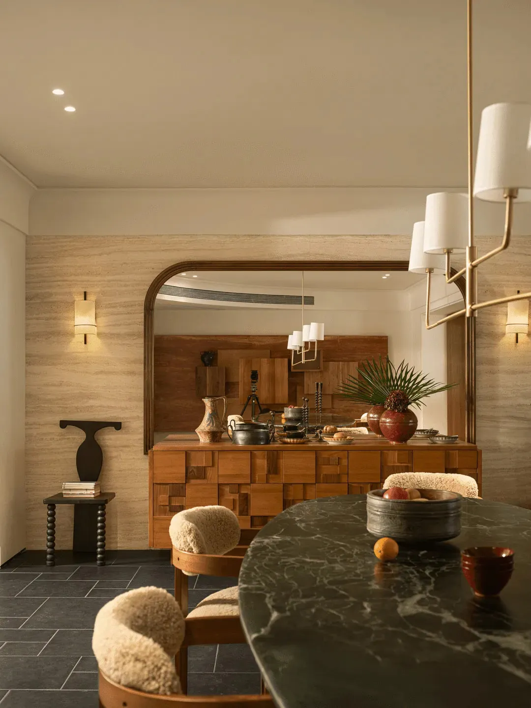 A modern kitchen with a black marble countertop, wooden cabinets, and a cozy atmosphere created by dim lighting, featuring a dining table, chairs, and various decorative items