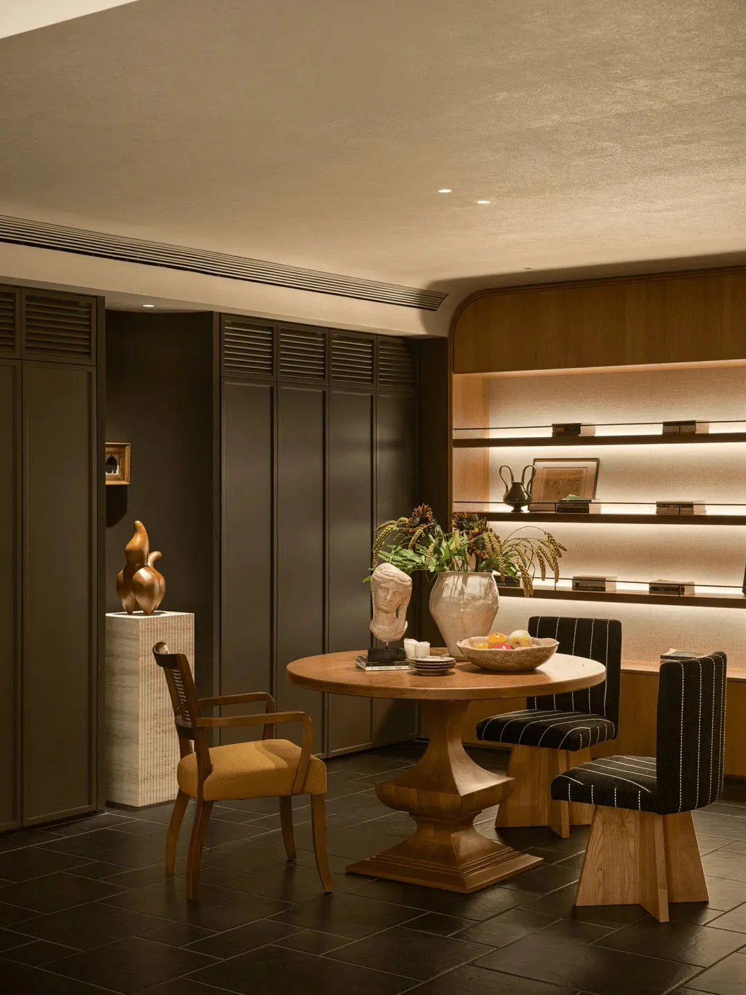 A well-lit living room with a wooden dining table, chairs, and a vase, surrounded by a couch and a chair, with natural light coming in through the windows