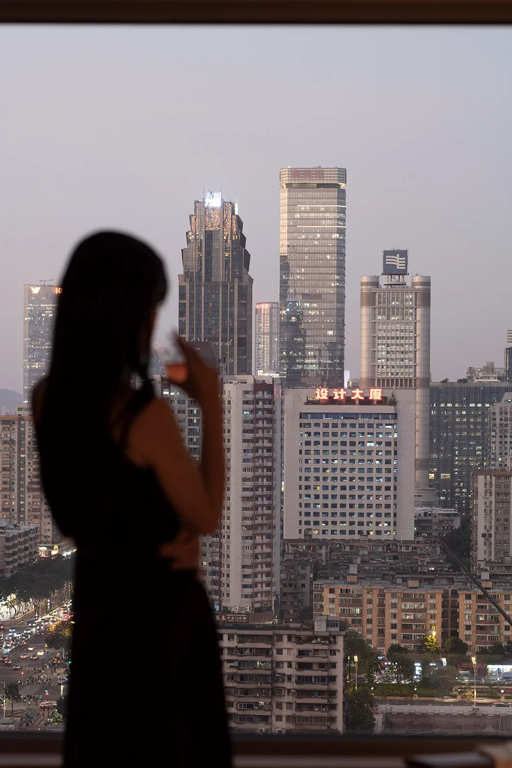 A woman stands on a rooftop at night, admiring the city's vibrant and lively atmosphere, illuminated by artificial lights
