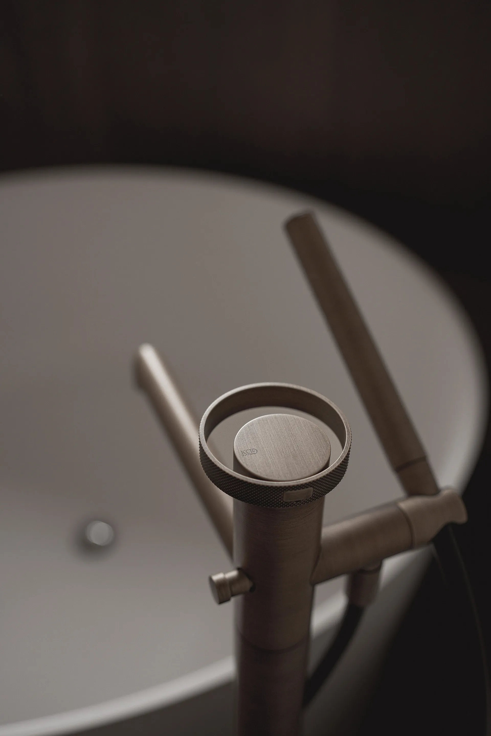 A modern bathroom with a white sink and a wooden faucet, set in a dimly lit space