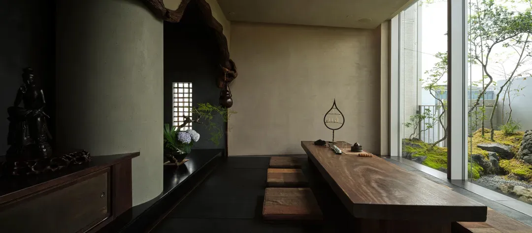 Rustic kitchen with a wooden table and benches, surrounded by a stone wall, with a vase on the table and dim lighting