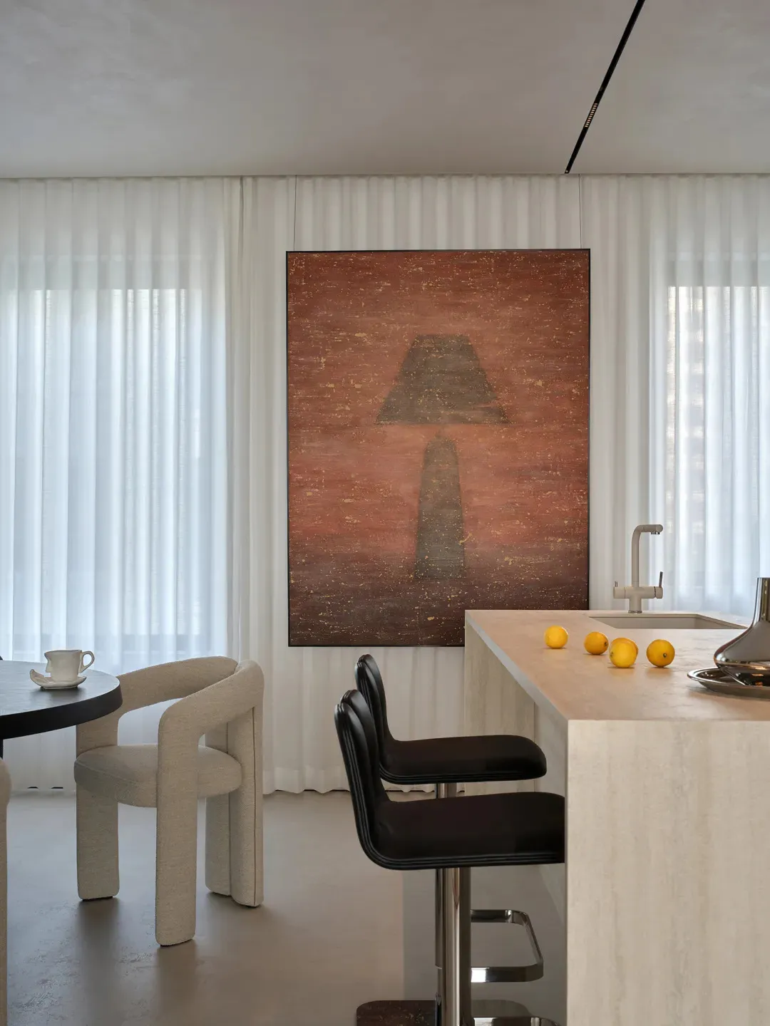A modern kitchen and dining area with a marble countertop, white walls, a black chair, and a large painting on the wall, set in a warm and inviting dimly lit space