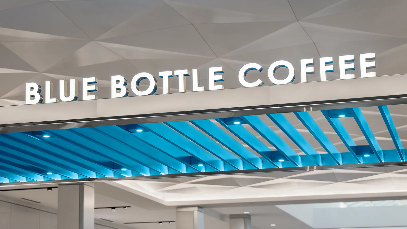 A modern coffee shop with a blue and white color scheme, featuring a large blue sign, a dining table, chairs, and a couch in a brightly lit space