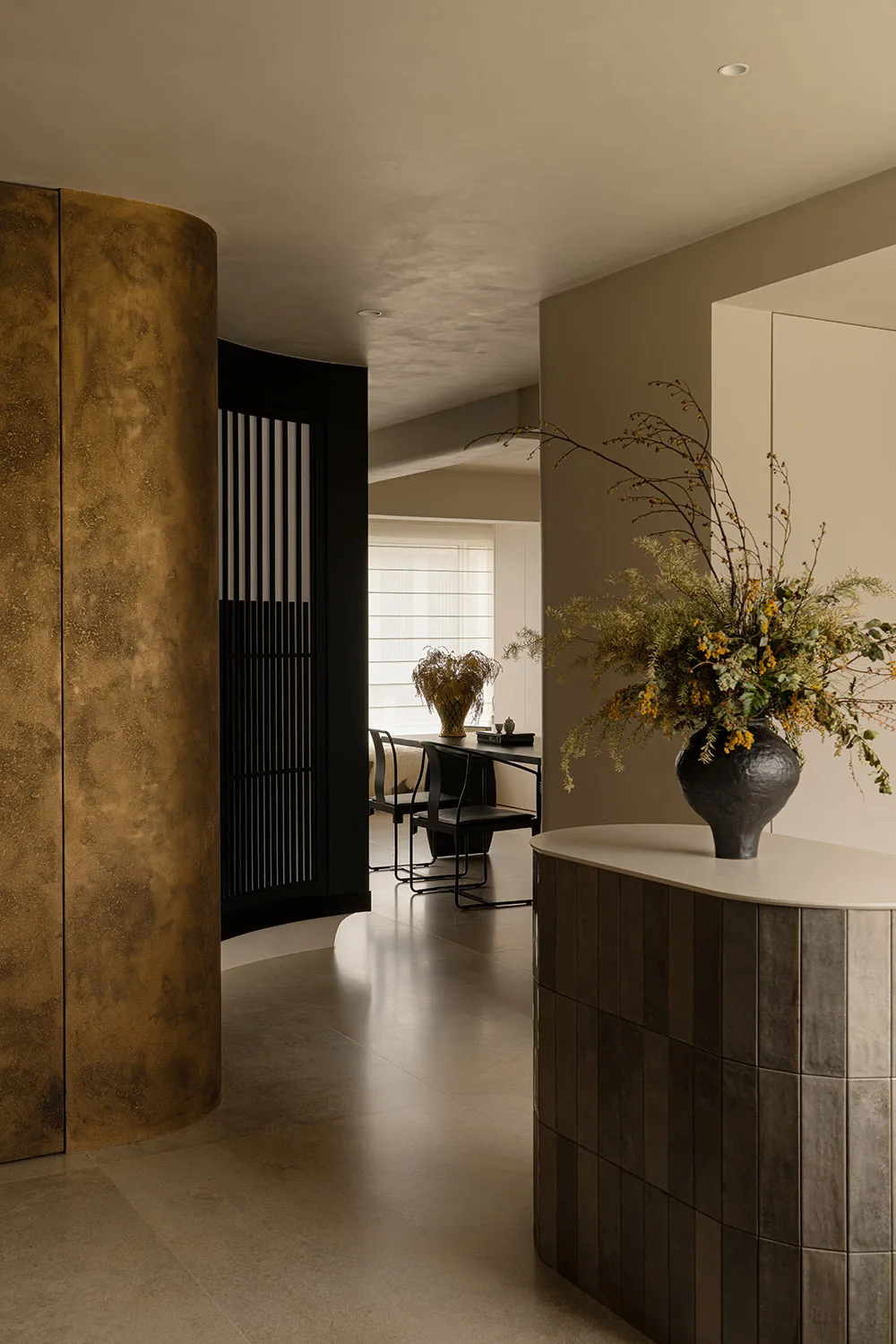 Sophisticated living space with a black and gold color scheme, a large window, a dining table, and a vase with flowers