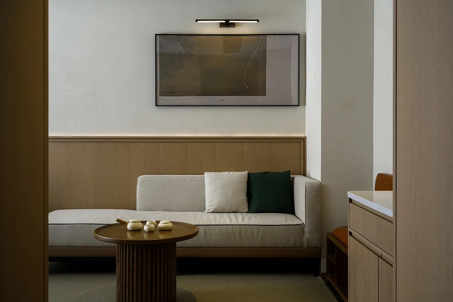 Cozy living room with a white couch, a brown chair, a wooden floor, and a painting on the wall, lit by dim lighting