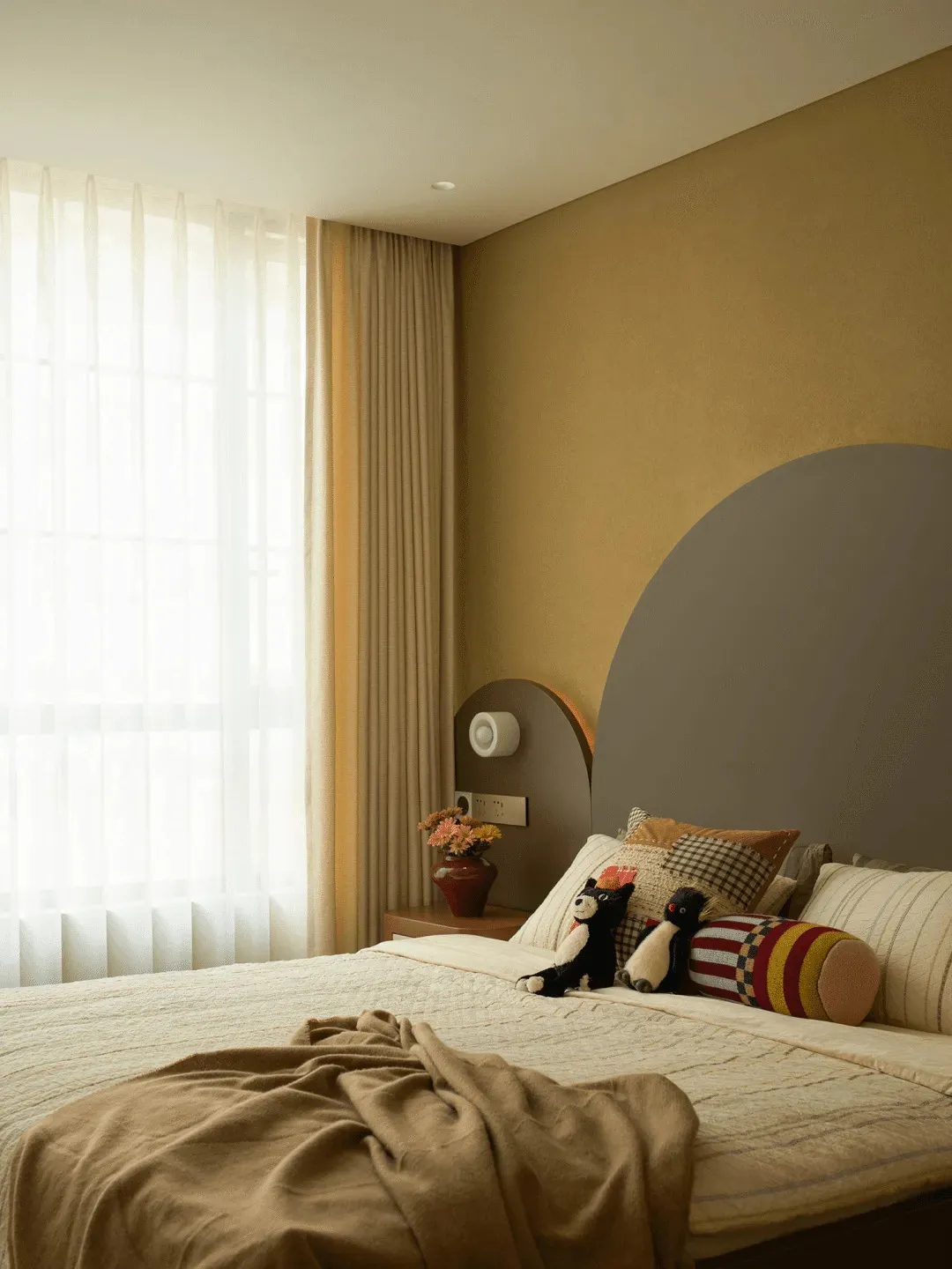 Cozy bedroom with a bed, mirror, and window, featuring a yellow wall, a blanket, pillows, and stuffed animals