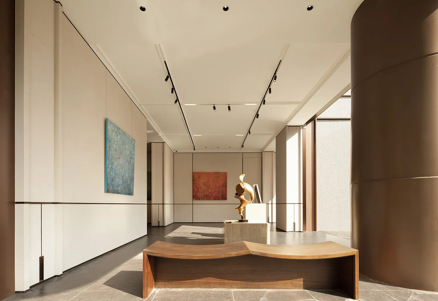A large, open room with a wooden floor, featuring three paintings on the walls and a sculpture on a pedestal, in a contemporary style with a focus on art pieces and open layout