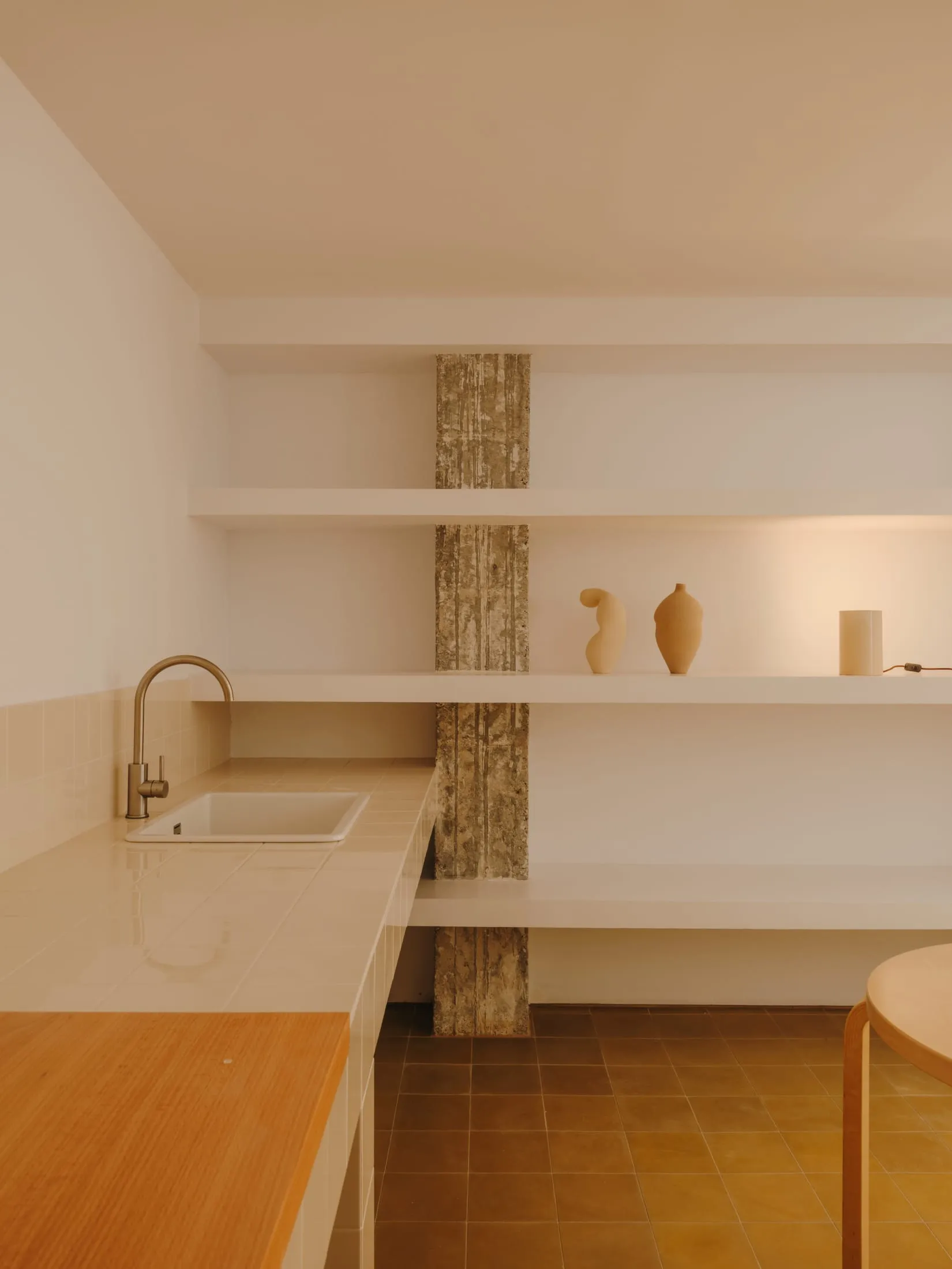 A well-organized kitchen with white cabinets, a tile floor, and wooden shelves, featuring vases and a bowl, with a focus on functionality and simplicity