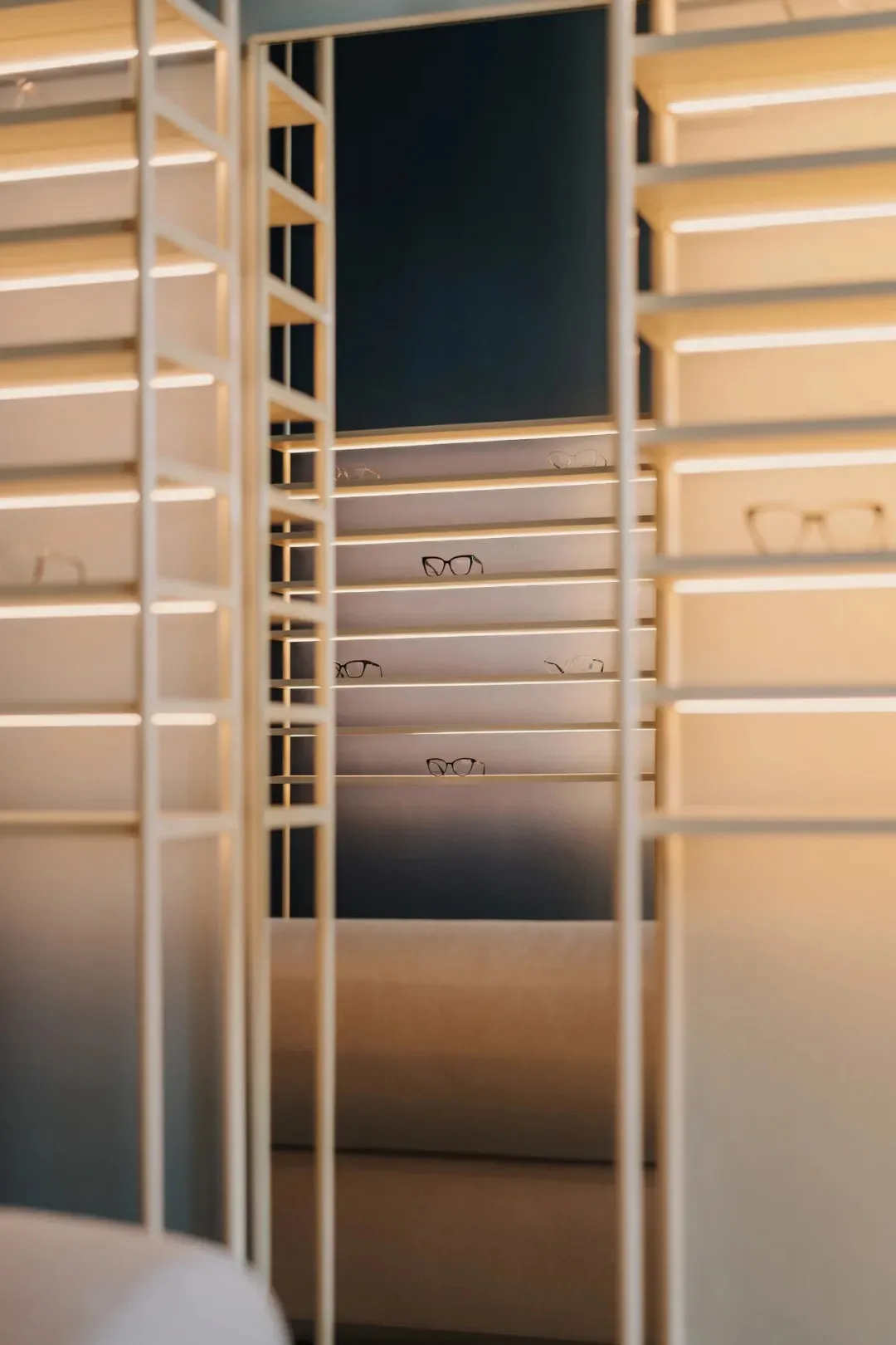 A store or showroom with a display case featuring glass shelves and various glasses on them, under soft and diffused lighting