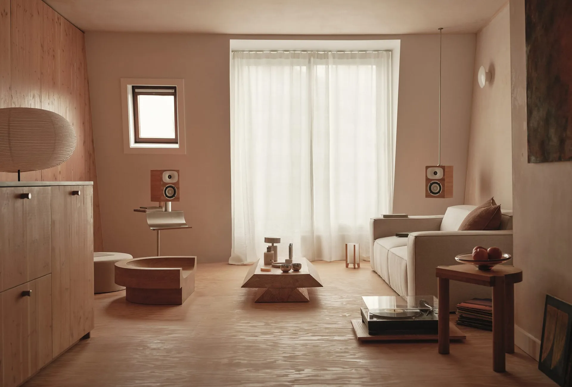 Modern living room with a large window, natural light, a couch, coffee table, chair, and speakers in a clean and organized space with white materials