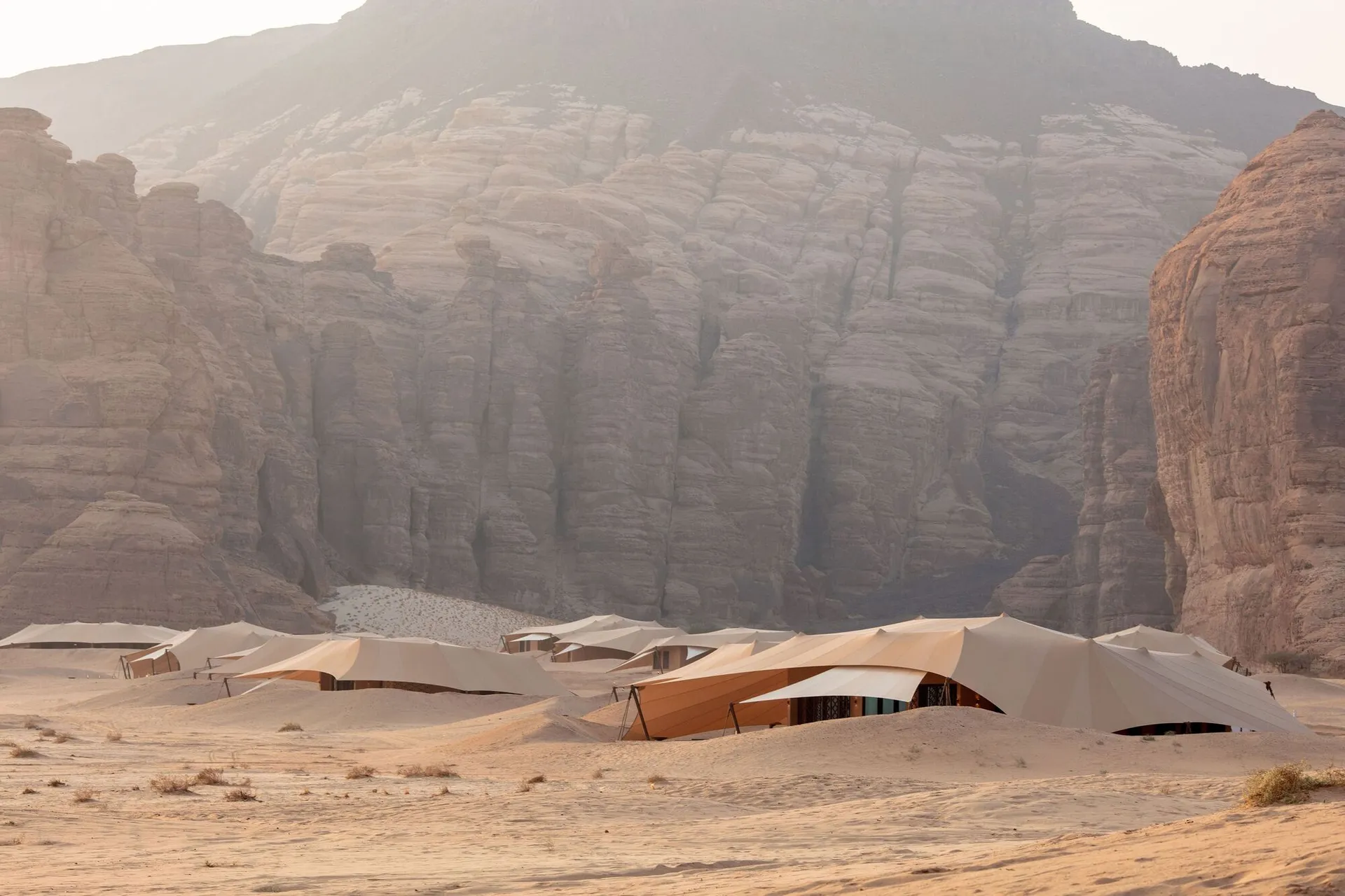 A desert landscape with a mountain in the background, featuring several tents of varying sizes and angles, creating a sense of depth and complexity