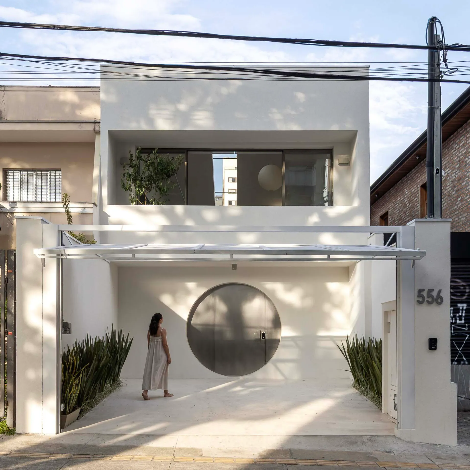 A modern white house with a circular window on the front, surrounded by a well-maintained garden