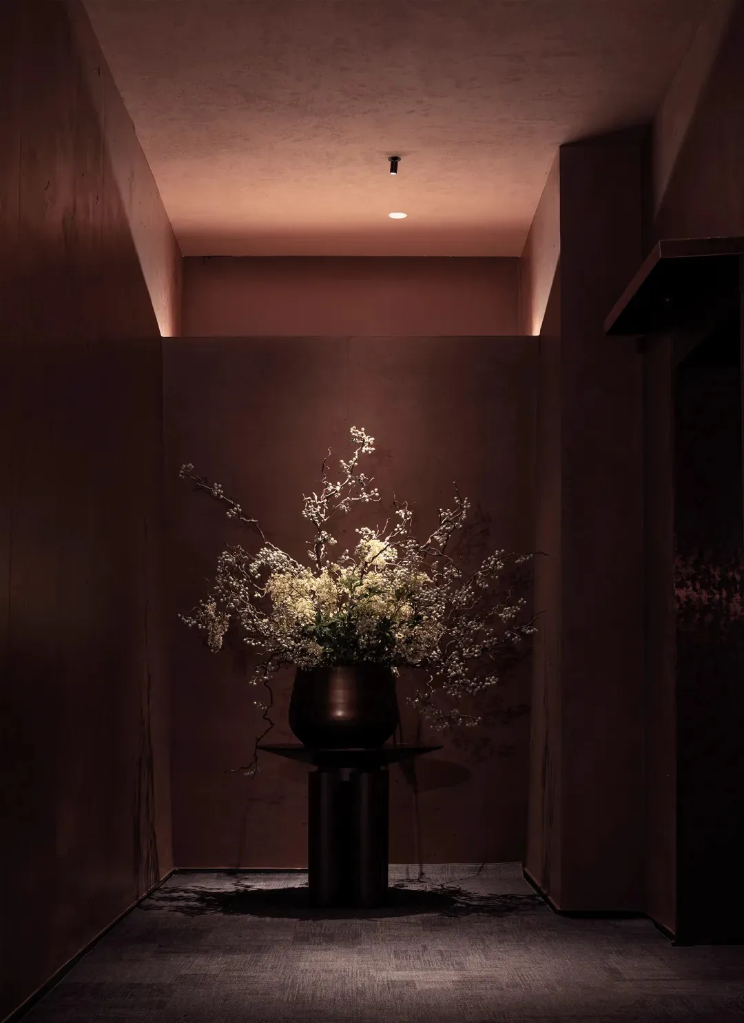 A small, dimly lit room with a brown color scheme, featuring a vase with flowers on a table as the main focus