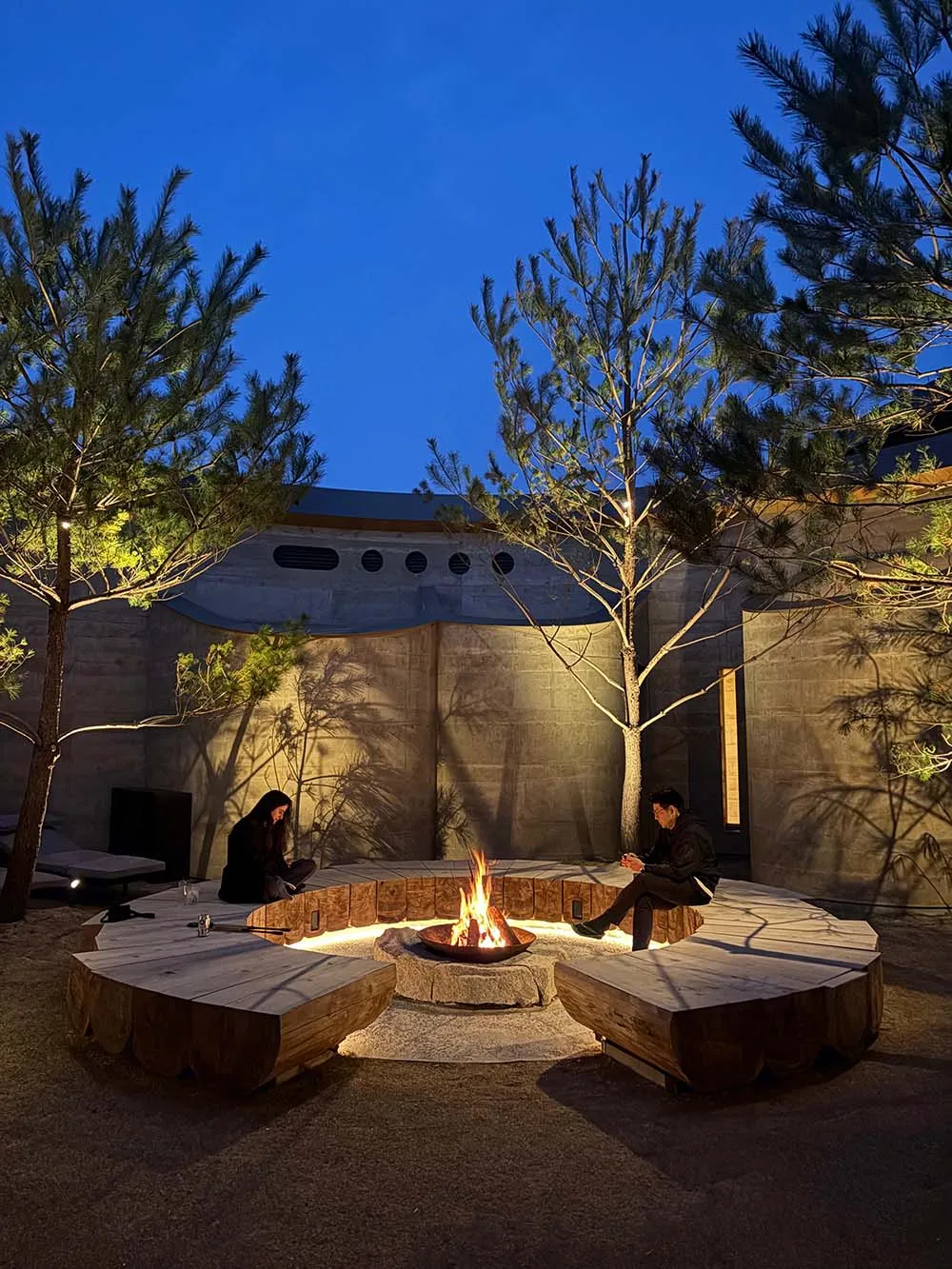 Cozy living room with a stone wall, stone floor, and a fireplace surrounded by a circle of stones, featuring a round table and seating for socializing and relaxation