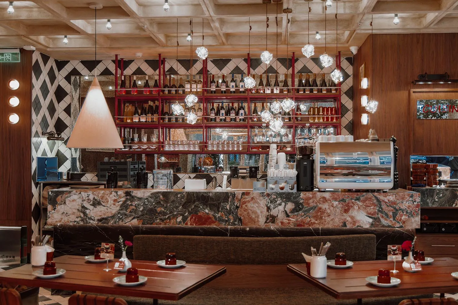 Modern restaurant interior with a marble bar, wooden elements, and dim lighting, featuring tables and chairs for guests