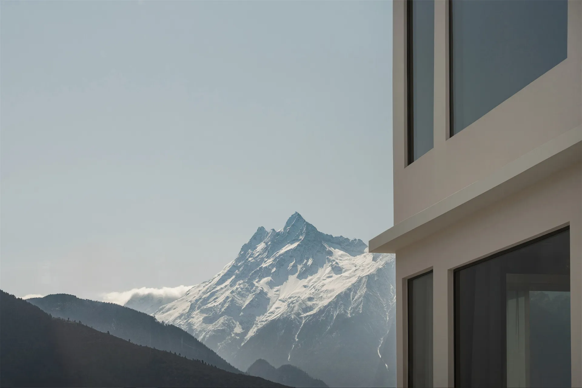 一座現代建築，外牆為混凝土，背景為藍天與覆雪的山峰