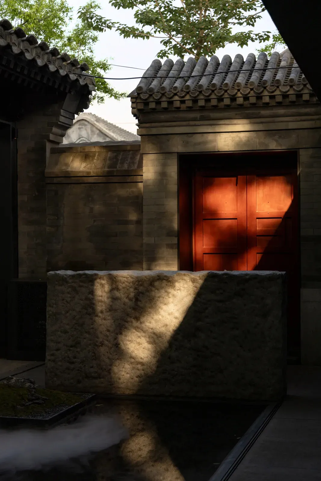 A stone door with an archway and stone wall in the background, set in an outdoor area with natural sunlight creating a warm atmosphere