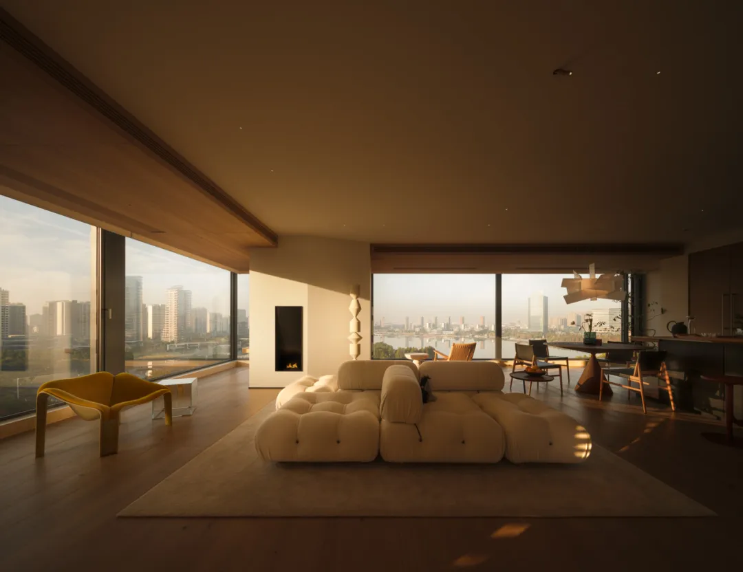 A modern living room with a large white couch, a fireplace, and a dining table, surrounded by various chairs and a potted plant, with natural light streaming in through the windows