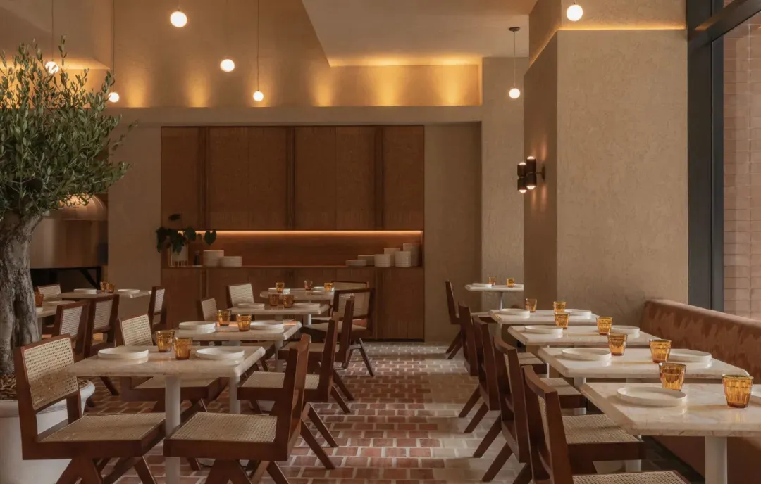 Warm and inviting dining space with tables, chairs, orange napkins, and wine glasses, featuring a combination of wood and brick elements