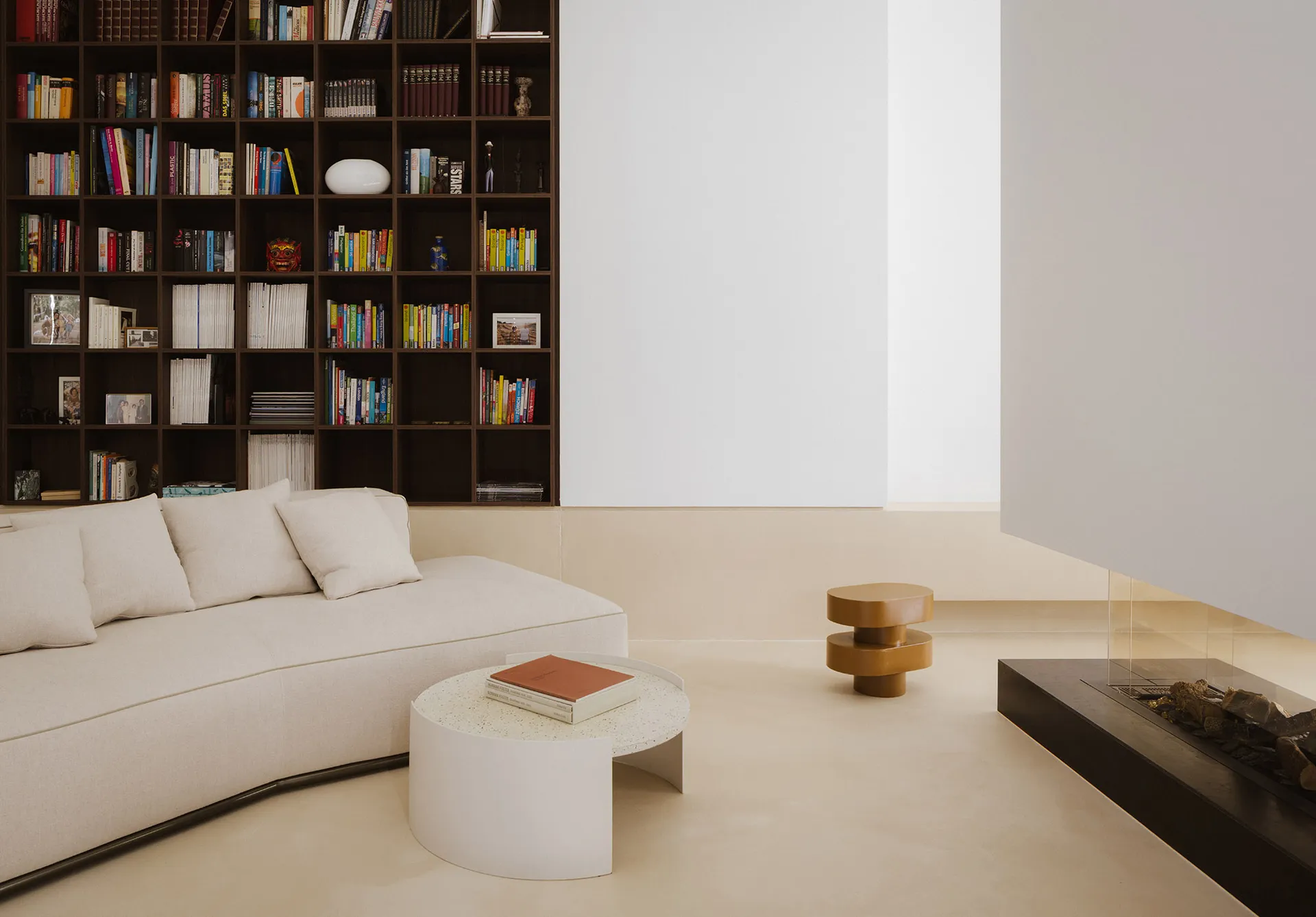 Cozy modern living space with a white color scheme, a couch, a chair, and a bookshelf, lit by natural light from a window